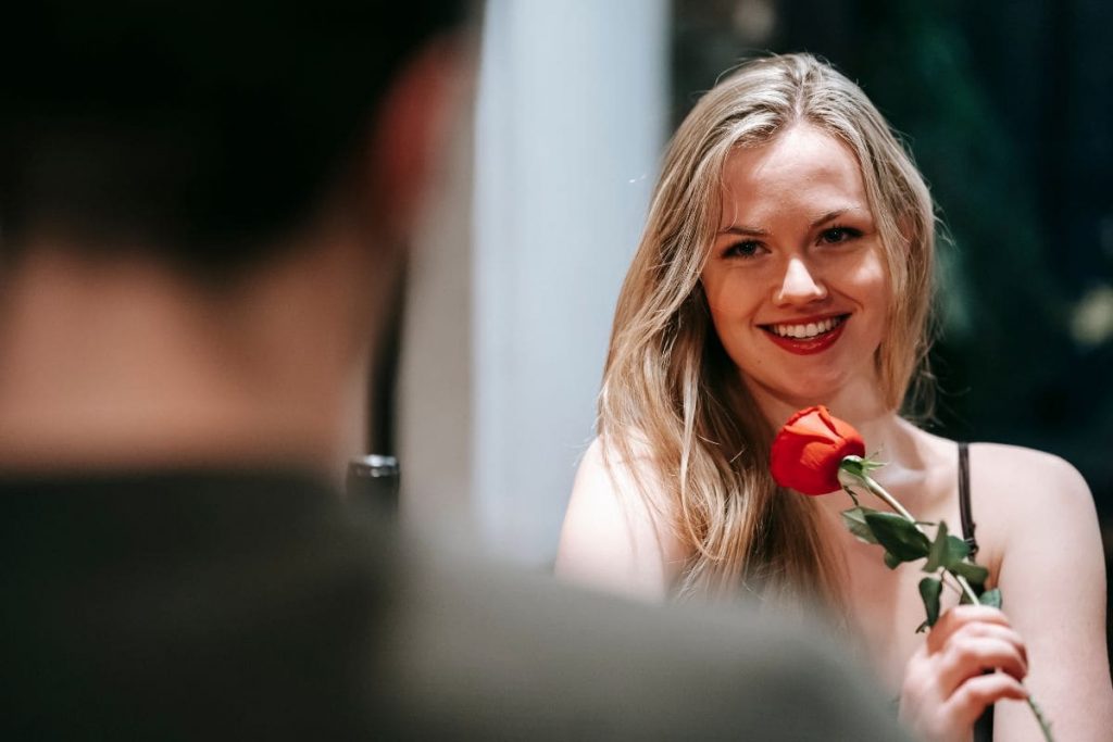 Beautiful blond woman holding red rose on a romantic date