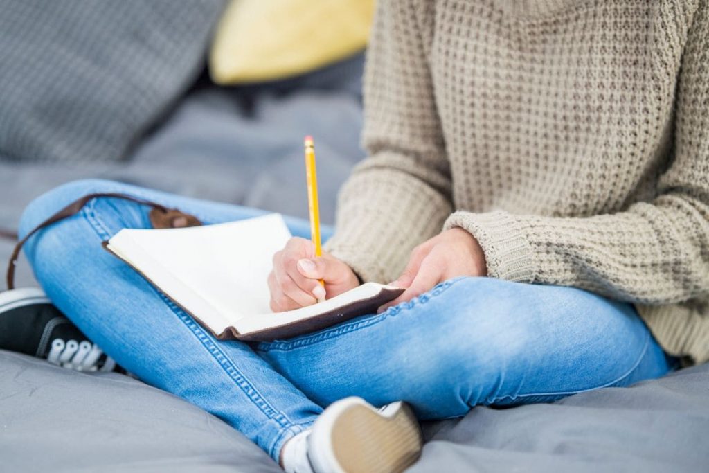 Woman in jeans and sweater sitting and writing a journal