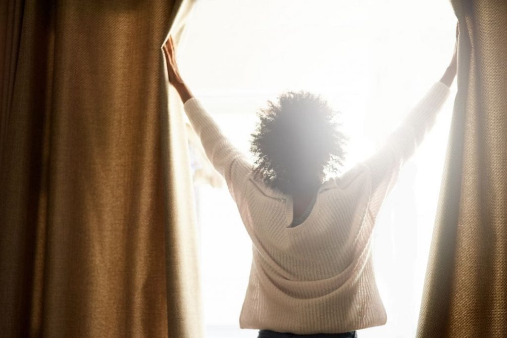 New day, new possibilities. Woman with black curly hair opening the curtains.