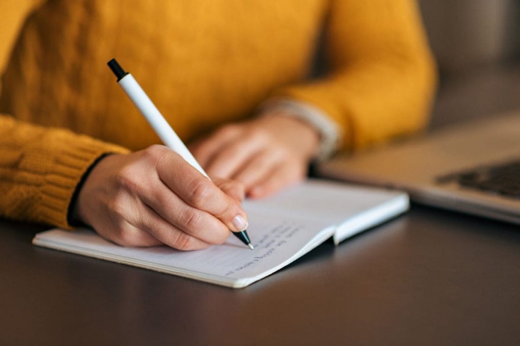 Woman in yellow sweater, writing in notebook. Close-up.