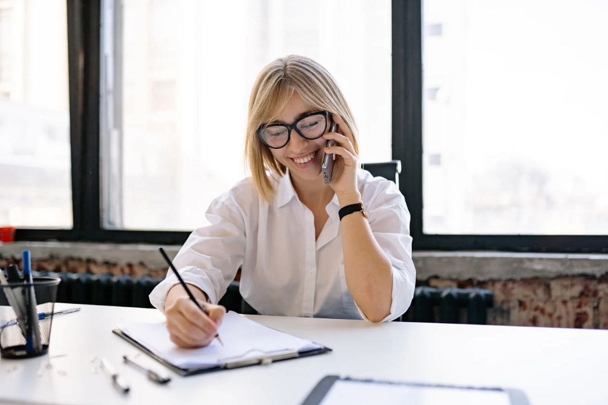 A blond woman taking notes while in a phone call