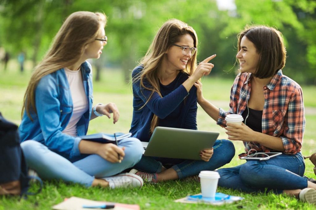 Three girls sitting on grass, interaction, talking, having fun