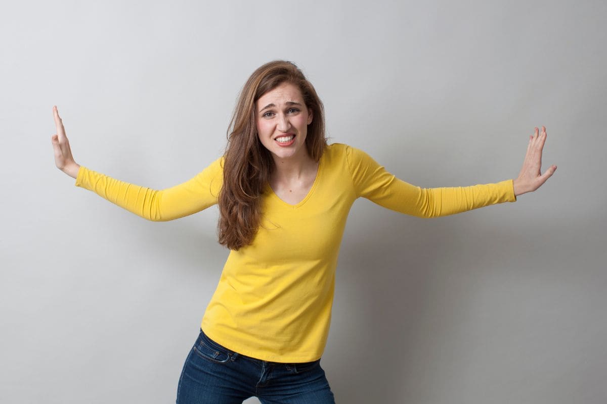 Pushing away hand gesture for angry beautiful young woman, yellow shirt and jeans