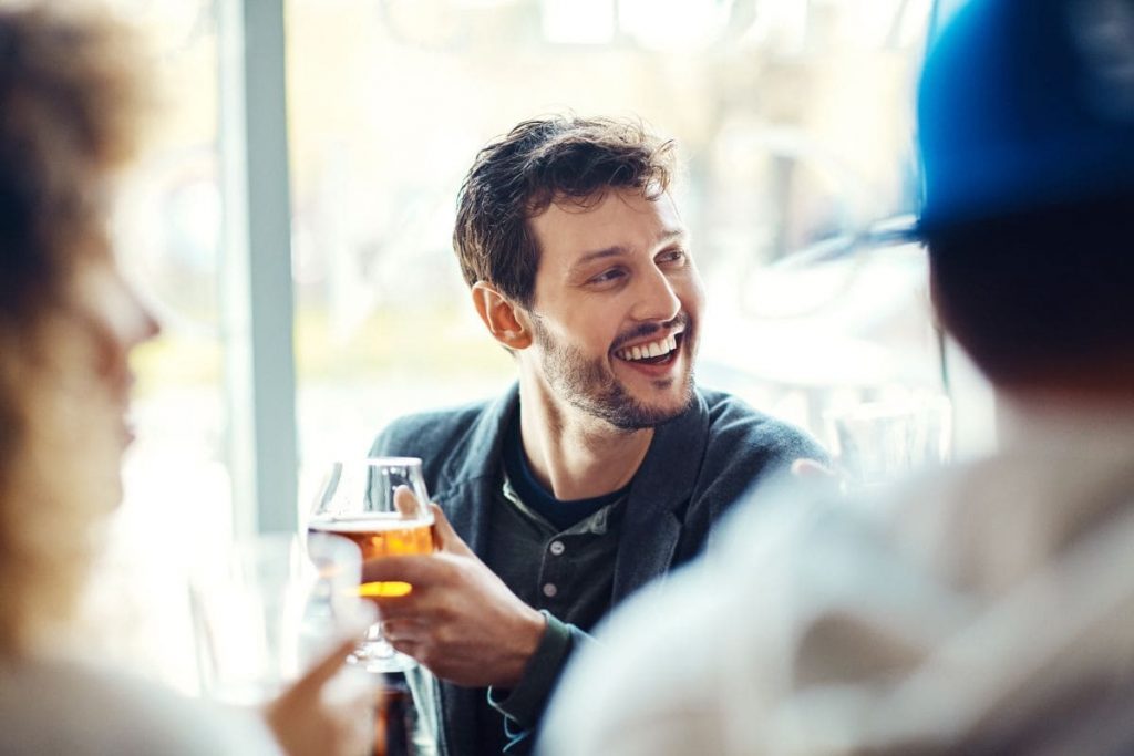 Man smiling holding a glass of beer, he's one sociable guy