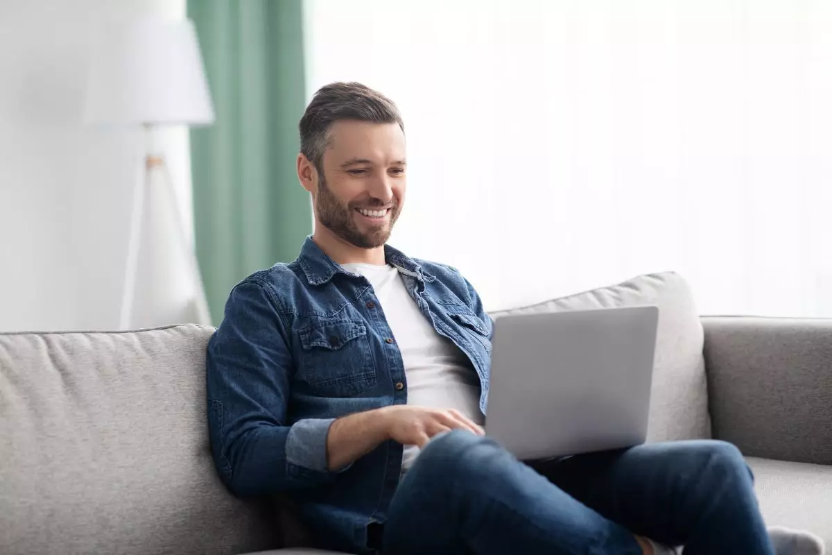 Smiling man using laptop, having a part time job, working from home