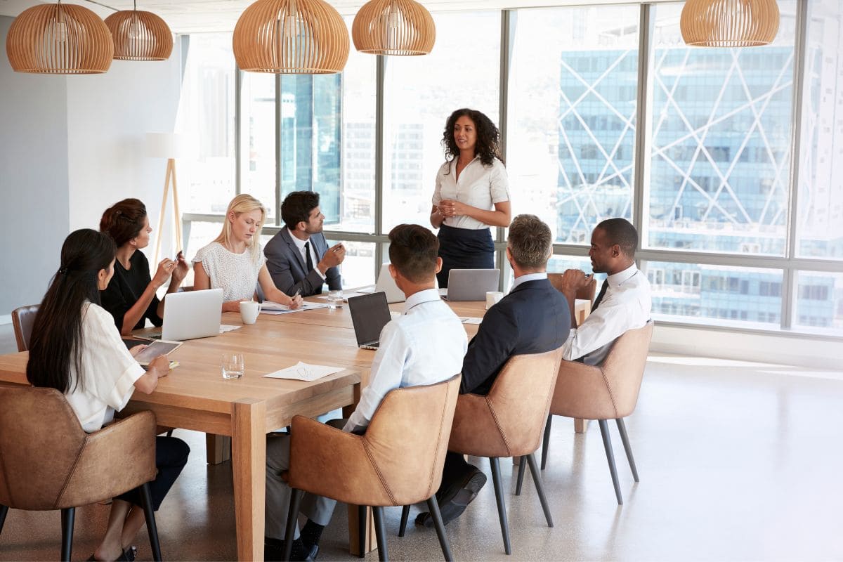 Meeting around board table, woman standing up in front of coworkers